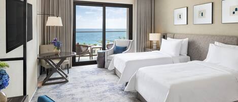 Habitación de hotel con dos camas, un escritorio, una silla y vista al océano.