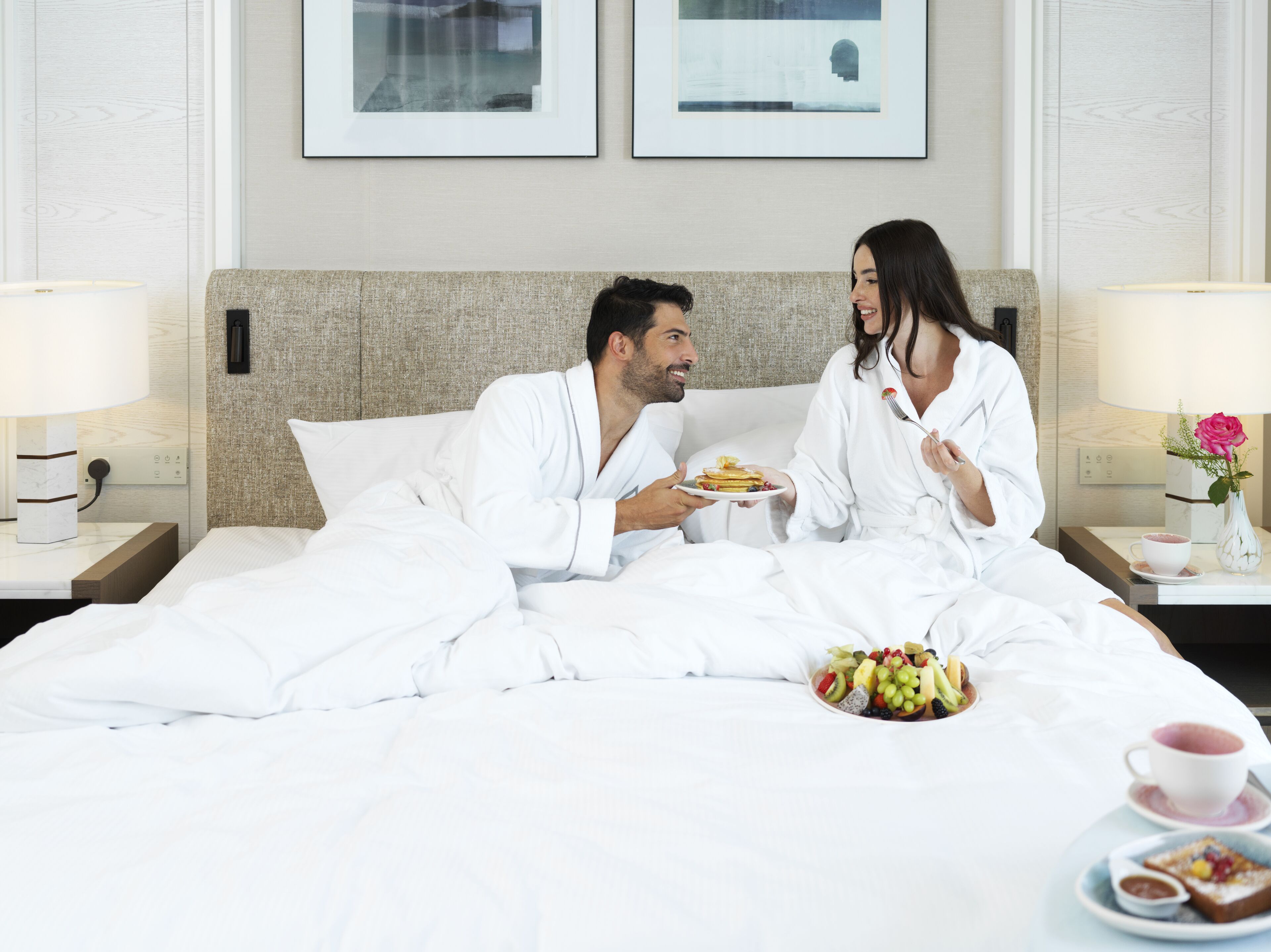 Een hotelkamer met een bed, een nachtkastje met een lamp en een aan de muur hangend fotolijstje.