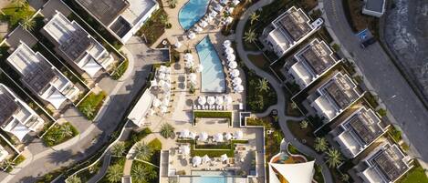Vue aérienne d’un complexe hôtelier doté de plusieurs piscines, de chaises longues et de palmiers.