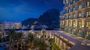 A modern hotel with multiple floors, balconies, and a view of a mountainous landscape. - Address Beach Resort Fujairah (Al Aqah)
