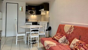 A compact living space with a kitchenette, a dining area with a white table and chairs, and a red sofa with patterned cushions.