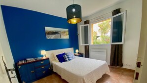 A bedroom with a bed, a nightstand, a dresser, a window with a view, and a hanging light fixture. - 3-bedroom Villa in Mèze with Garden and Air Conditioning (Mèze)