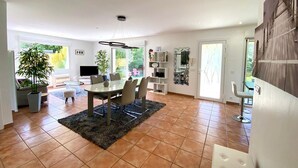 A spacious dining area with a large table and chairs, surrounded by a kitchen and a living area with a TV and shelves. - 3-bedroom Villa in Mèze with Garden and Air Conditioning (Mèze)