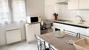 A modern kitchen with white cabinets, a microwave, a sink, and a dining area with chairs and a table. - Bright apartment in Bouzigues, 50m from beach, garden and parking (Bouzigues)