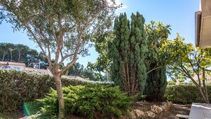 A landscaped garden with various trees and shrubs, a paved area, and a building in the background. - Bright apartment in Bouzigues, 50m from beach, garden and parking (Bouzigues)