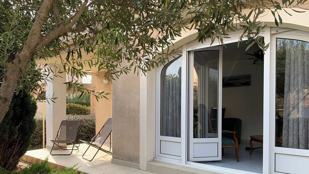 A covered outdoor seating area with two chairs, a table, and a glass door leading to an interior room. - Bright apartment in Bouzigues, 50m from beach, garden and parking (Bouzigues)