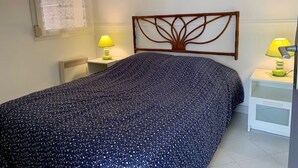 A bedroom with a bed, two bedside tables, a headboard with a tree design, a window with lace curtains, and a painting on the wall. - Bright apartment in Bouzigues, 50m from beach, garden and parking (Bouzigues)