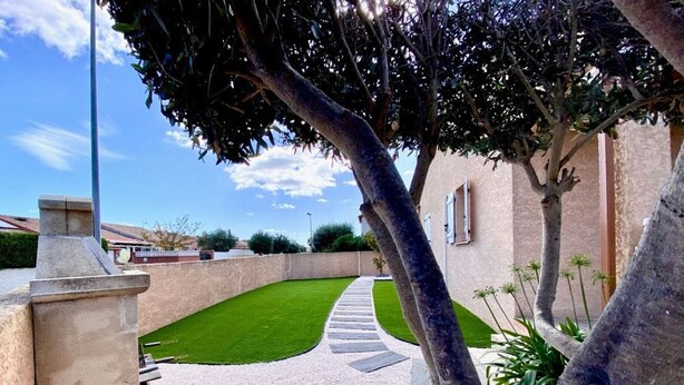A well-maintained garden with a gravel path leading to a house with a stone wall and a clear blue sky. - Air-conditioned house in Mèze with garden and private parking (Mèze)