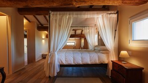 Quarto com cama de dossel, piso de madeira e mesa de cabeceira com abajur.