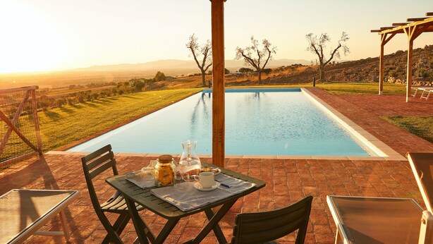 Uma área à beira da piscina com uma mesa posta para o café da manhã, vista para a piscina e uma estrutura de pérgola.