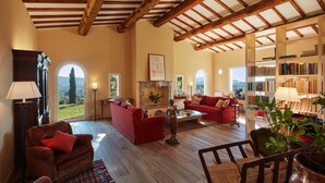 Uma sala de estar ampla com vigas de madeira, sofás vermelhos, uma lareira e uma estante de livros.