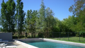 Una piscina con bordo in cemento, circondata da una recinzione in metallo e alberi.