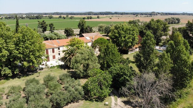 Una casa di campagna con tetto in tegole rosse, immersa nel verde e circondata da campi.