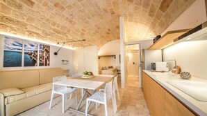 Une cuisine moderne avec un plafond en pierre, un coin repas avec une table et des chaises, et une vue sur la mer par une fenêtre.