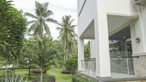 A modern building with a white exterior, a stone pathway, and lush greenery including palm trees and purple flowers. - Asoka Resort Banten (Panimbang)