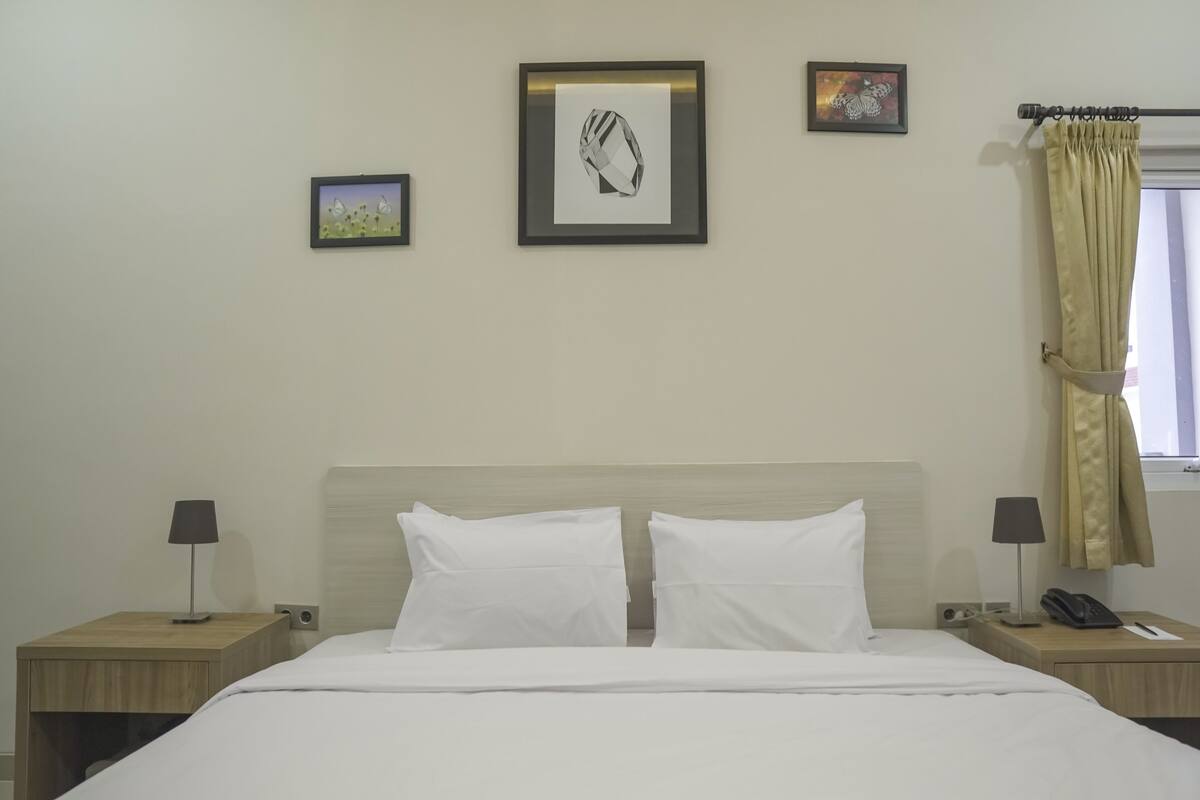 Une chambre d’hôtel avec un lit, deux tables de chevet avec des lampes, un téléphone et des tableaux encadrés accrochés au mur.