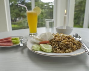 A table with a plate of food, a glass of orange juice, a candle, and a fork. - Asoka Resort Banten (Panimbang)