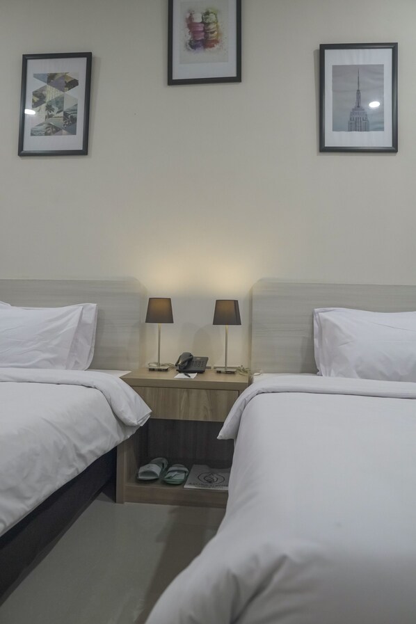 A hotel room with two beds, a nightstand with lamps, a phone, and slippers. - Asoka Resort Banten (Panimbang)