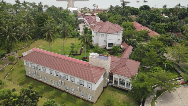 A large, multi-story building with a red-tiled roof, surrounded by lush greenery and palm trees. - Asoka Resort Banten (Panimbang)