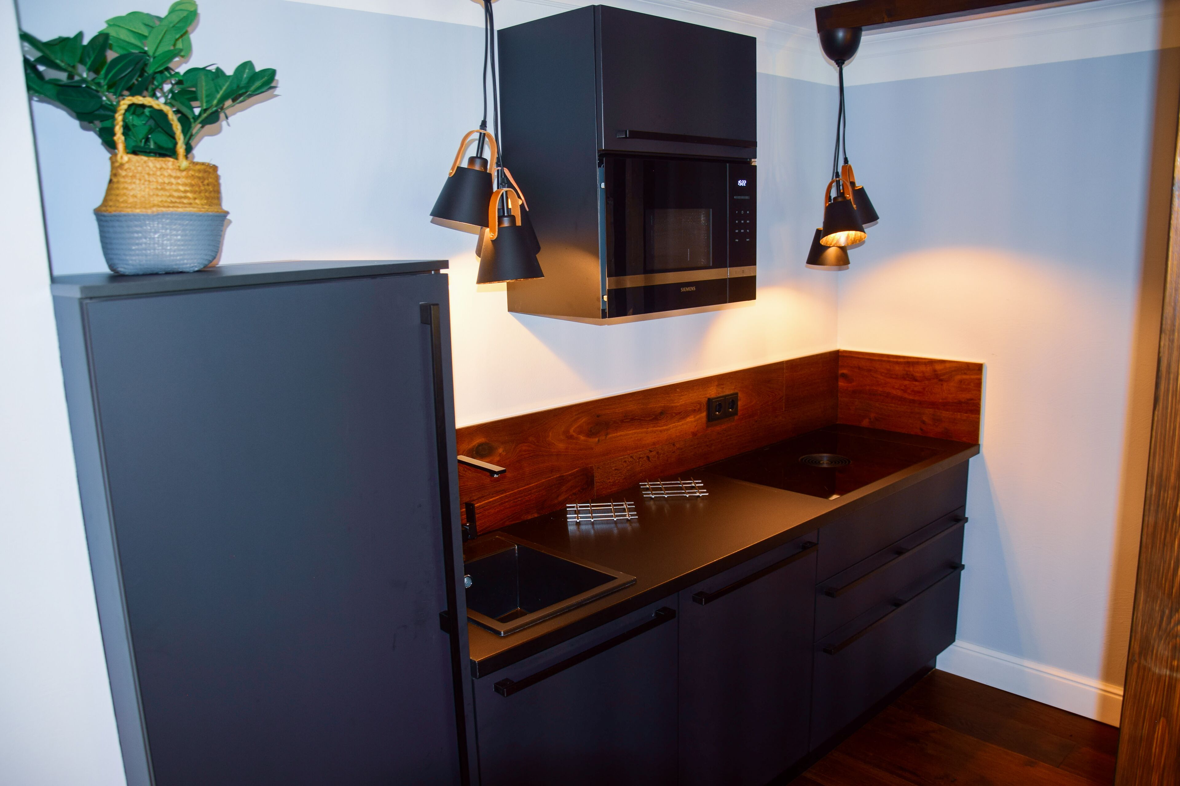 Une cuisine moderne avec un réfrigérateur noir, un four à micro-ondes en acier inoxydable et un plan de travail en bois.