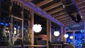 Una zona de bar con vigas de madera, estantes llenos de botellas e iluminación moderna.