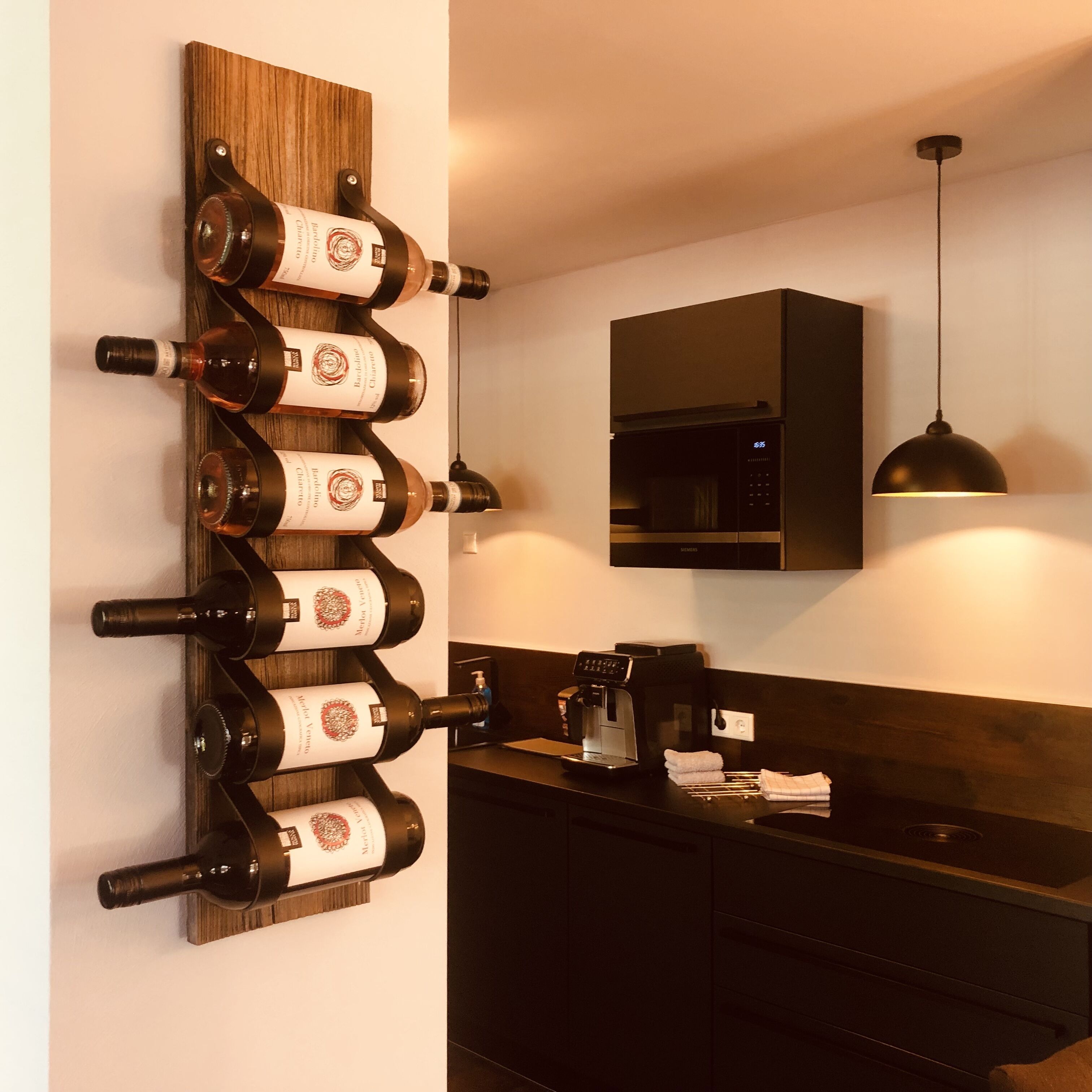 A modern kitchen with a wine rack holding several bottles, a coffee machine, and a hanging pendant light.