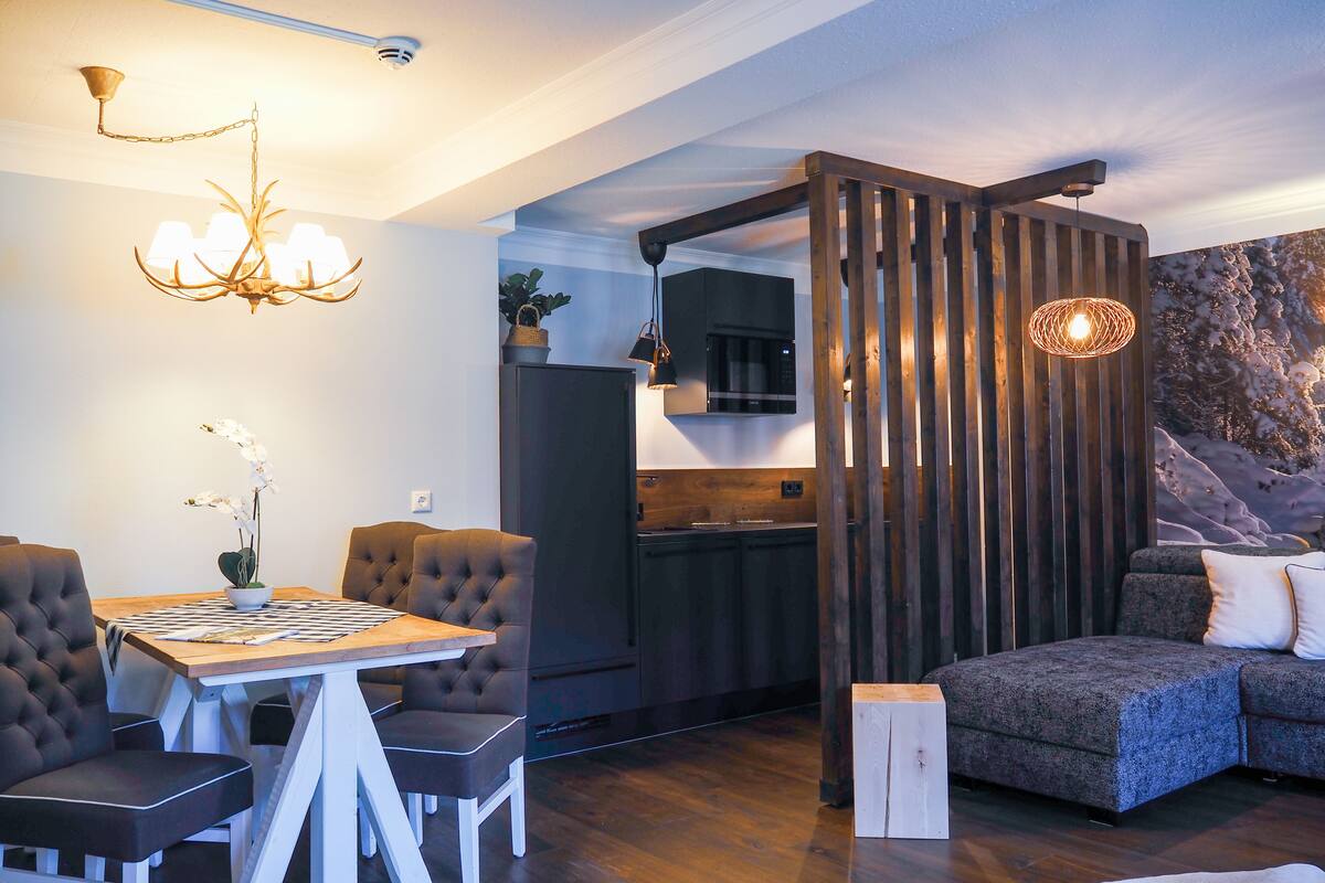 Una sala de estar moderna con comedor, cocina y un ventanal con vistas a árboles cubiertos de nieve.