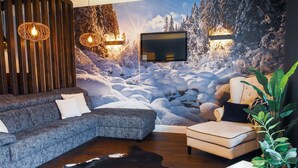 Una sala de estar moderna con un gran mural en la pared que muestra un paisaje nevado, un sofá seccional, un sillón beige pequeño, una mesa de centro con una revista y una planta en maceta.
