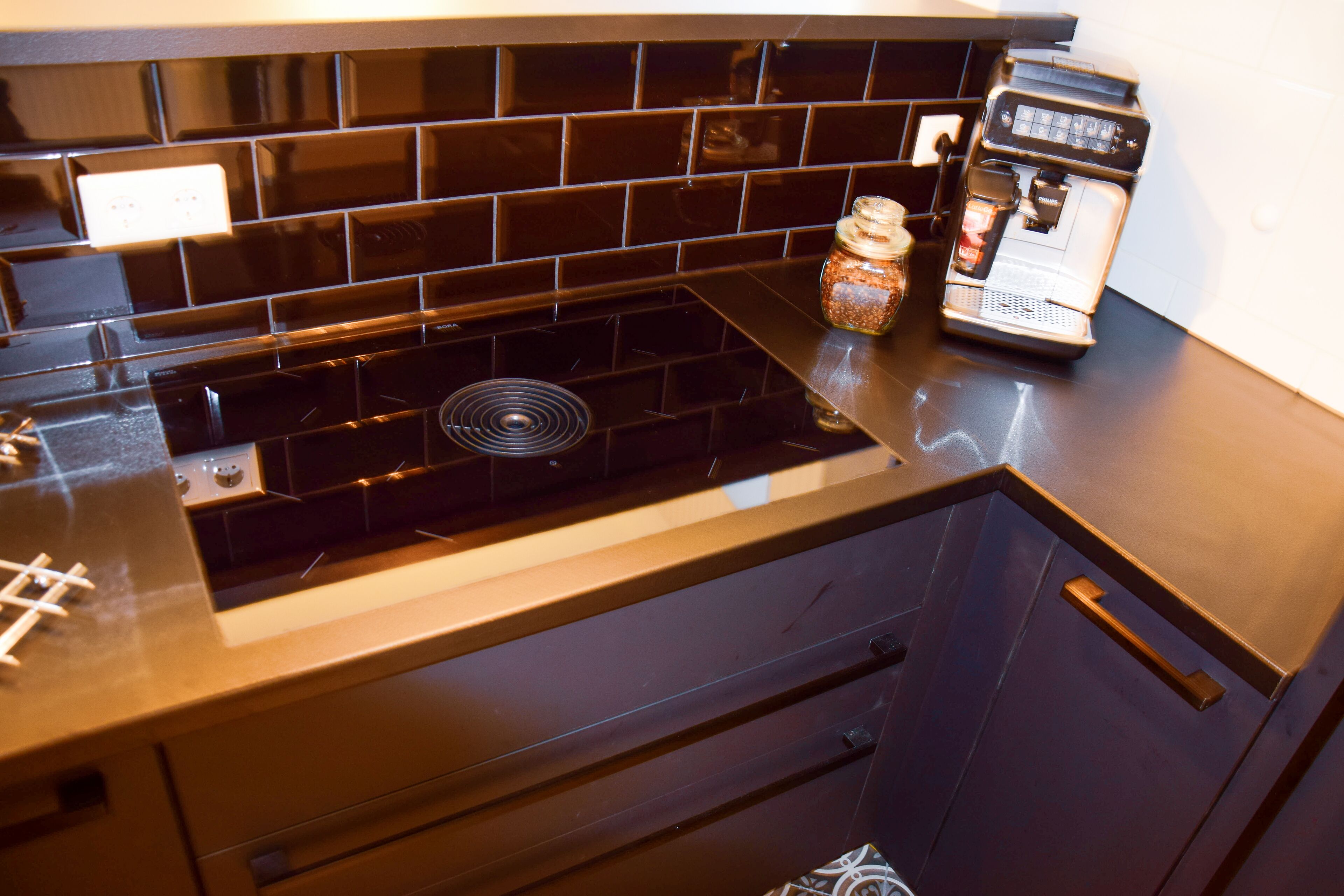 A kitchen with a black tiled backsplash, a built-in stove, a coffee machine, and a spice jar.