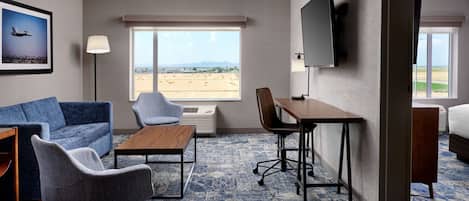 Une chambre d’hôtel dotée d’une grande fenêtre, d’un canapé, d’un fauteuil, d’un bureau et d’un téléviseur à écran plat.