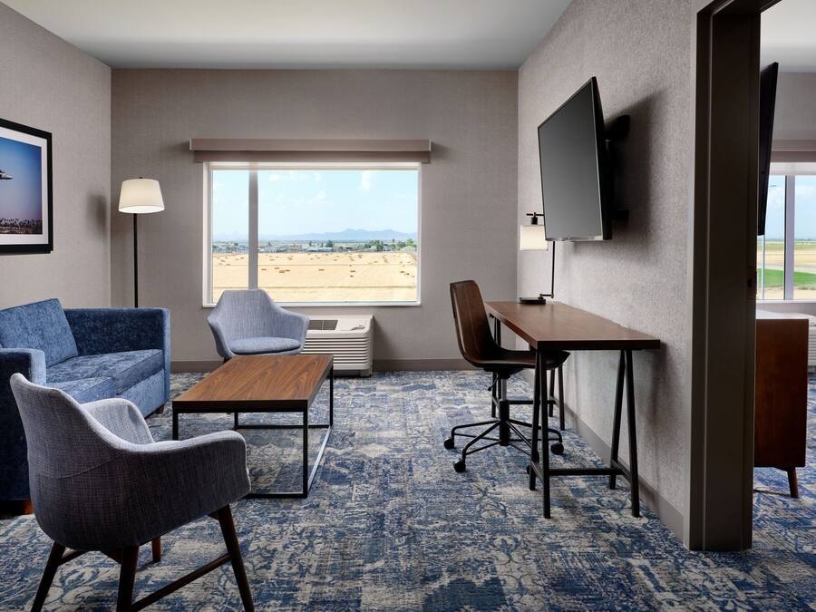 A hotel room with a large window, a sofa, a chair, a desk, and a flat-screen TV.
