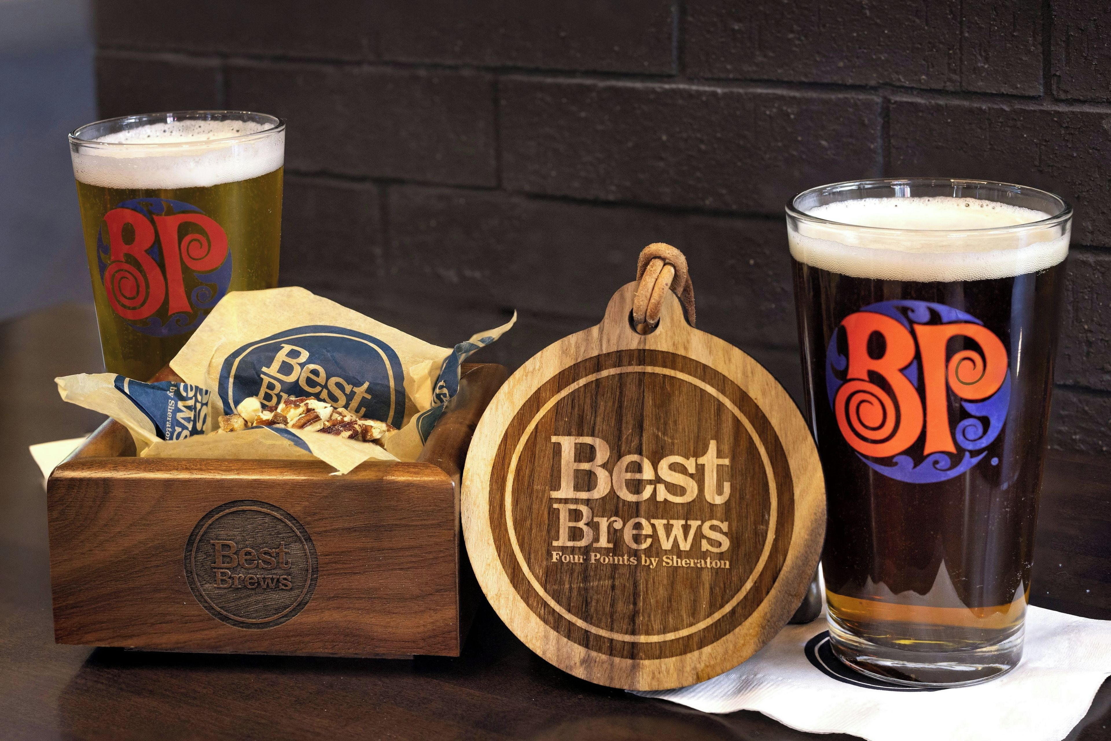 Un posavasos de madera con la marca 'Best Brews', una caja de madera con la marca 'Best Brews' y 'Four Points by Sheraton', y dos vasos de cerveza con la marca 'Best Brews'.