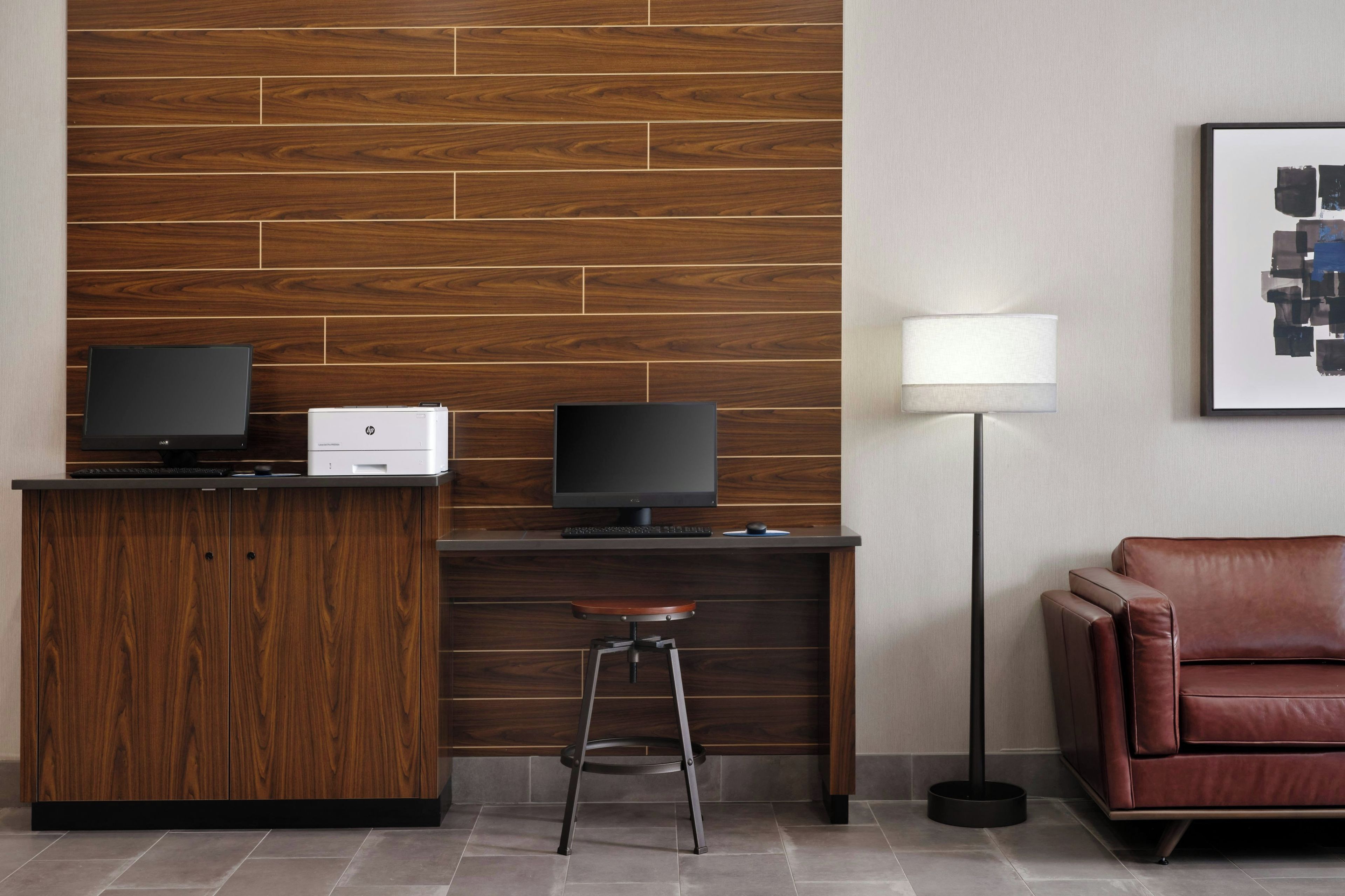 A modern reception desk with two monitors, a printer, and a stool.