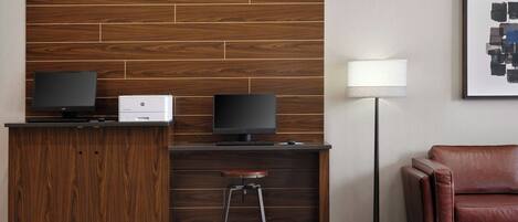 A modern reception desk with two monitors, a printer, and a stool.