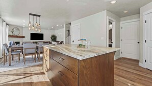A modern kitchen with a large island, wooden cabinets, and a dining area with a table and chairs. - Modern Farmhouse Retreat | 5BR | With Pool Views (Meridian)