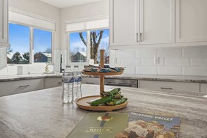 A kitchen with white cabinets, a marble countertop, a water dispenser, a tray with snacks, and a brochure on the counter.