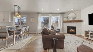 A living room with a fireplace, a dining area with a table and chairs, and a kitchen in the background. - Modern Farmhouse Retreat | 5BR | With Pool Views (Meridian)
