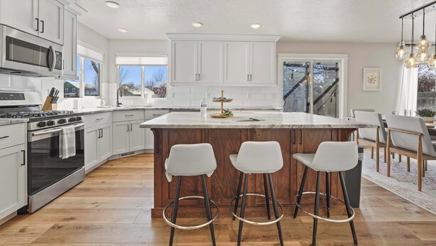 A modern kitchen with white cabinets, a central island with stools, a large window, and a staircase leading to another level. - Modern Farmhouse Retreat | 5BR | With Pool Views (Meridian)