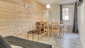 A cozy room with a wooden wall, a dining table with chairs, a small round table, and a sofa.