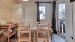 A dining area with a wooden table and chairs, a white refrigerator, and a window with curtains.