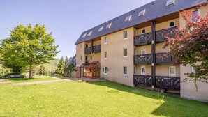 A multi-story building with balconies, a covered entrance, and a well-maintained lawn. - Direct access to the slopes - flat for 4 (Genos)
