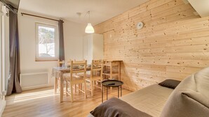 A cozy room with a wooden wall, a dining table with chairs, a sofa, and a hanging light fixture. - Direct access to the slopes - flat for 4 (Genos)