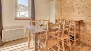 A dining area with a table set for two, wooden chairs, a white cabinet, and a window with a view of trees. - Direct access to the slopes - flat for 4 (Genos)