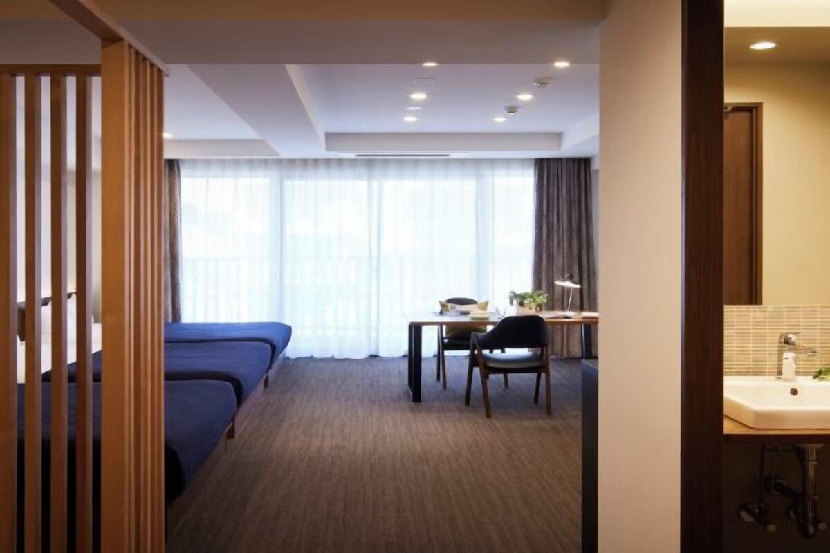 A hotel room with a bed, a desk, a chair, and a bathroom with a sink.