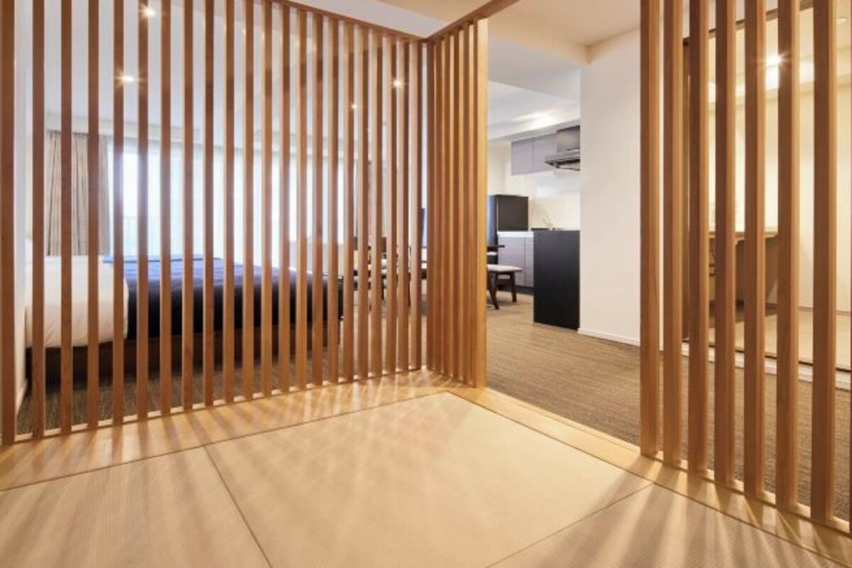 A modern hotel room with a wooden partition, a bed, and a desk area.