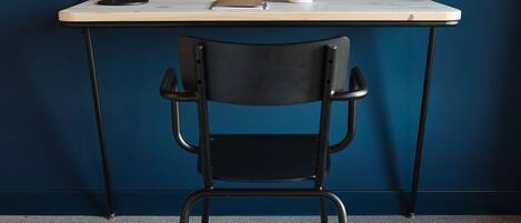 Un escritorio con lámpara, taza y silla frente a una pared azul.