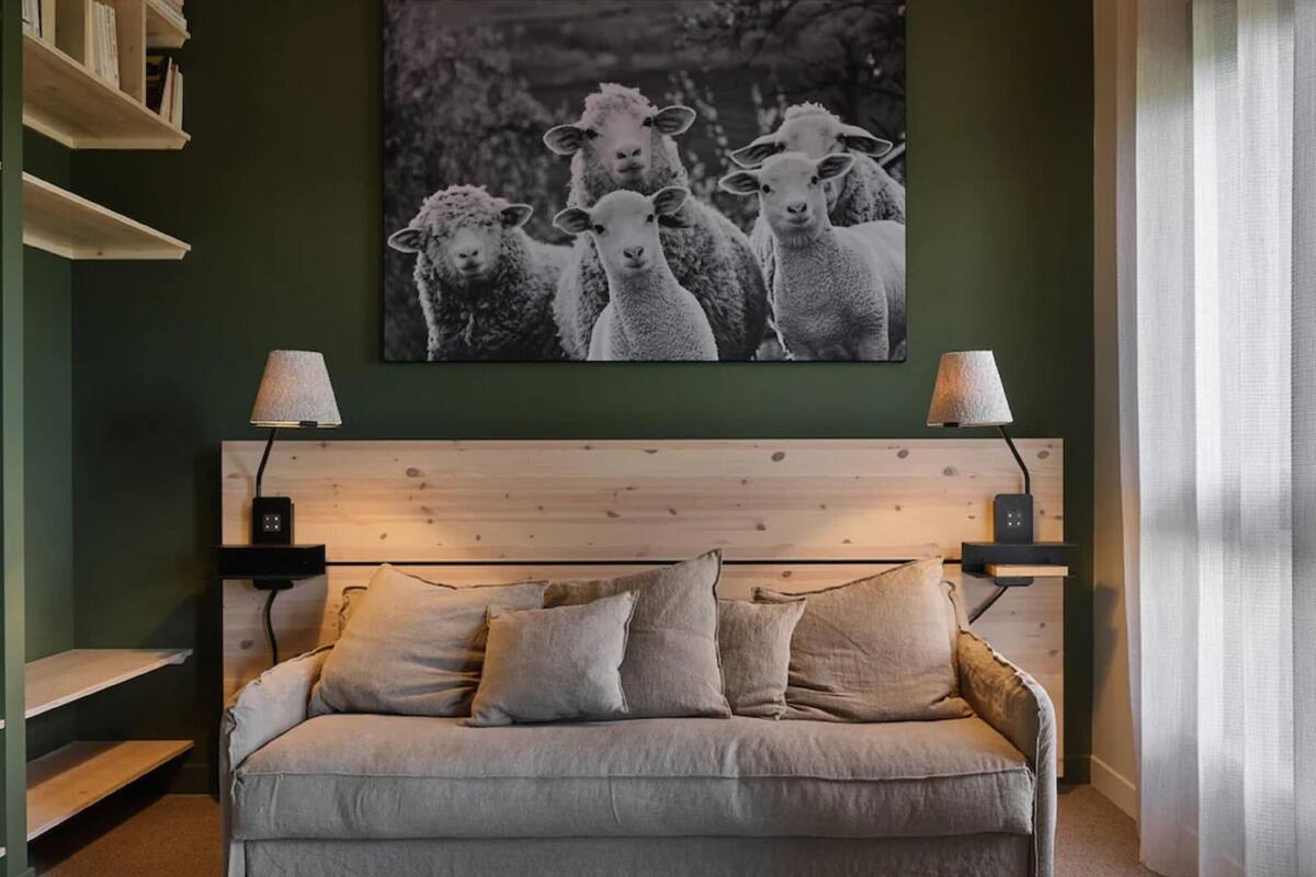 A cozy room with a wooden headboard, a grey sofa with multiple cushions, and a black and white photograph of sheep on the wall.