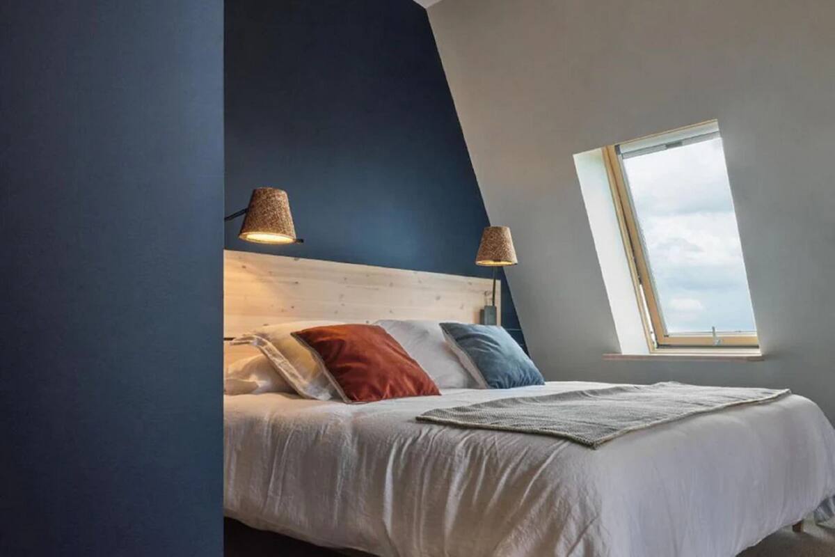 A bedroom with a wooden headboard, two bedside lamps, a large window, and a bed with multiple pillows.