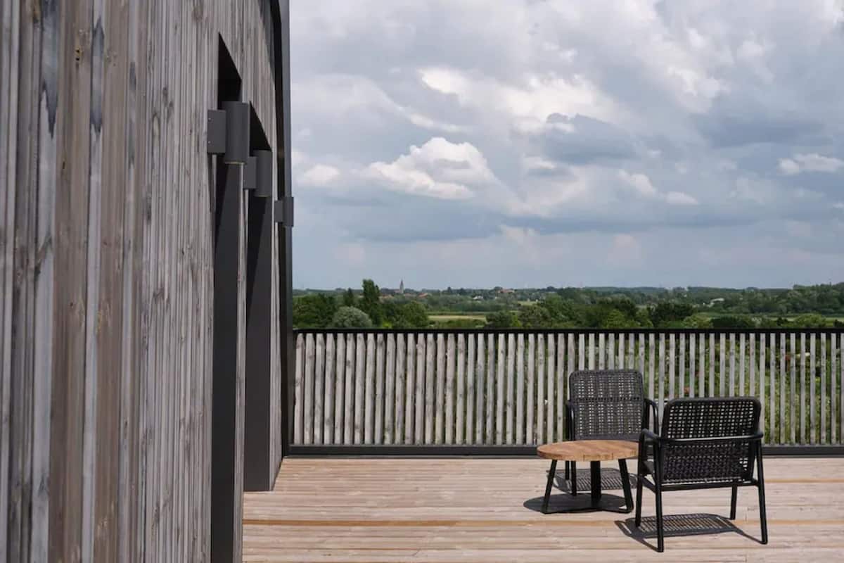 A wooden deck with a view of a rural landscape, two black chairs, and a small table.