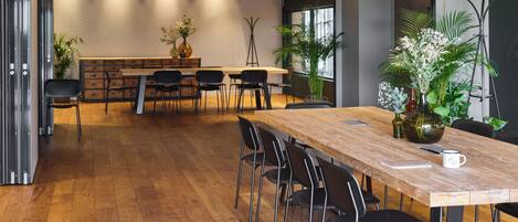 Una amplia sala de conferencias con una larga mesa de madera, sillas negras y plantas en macetas.